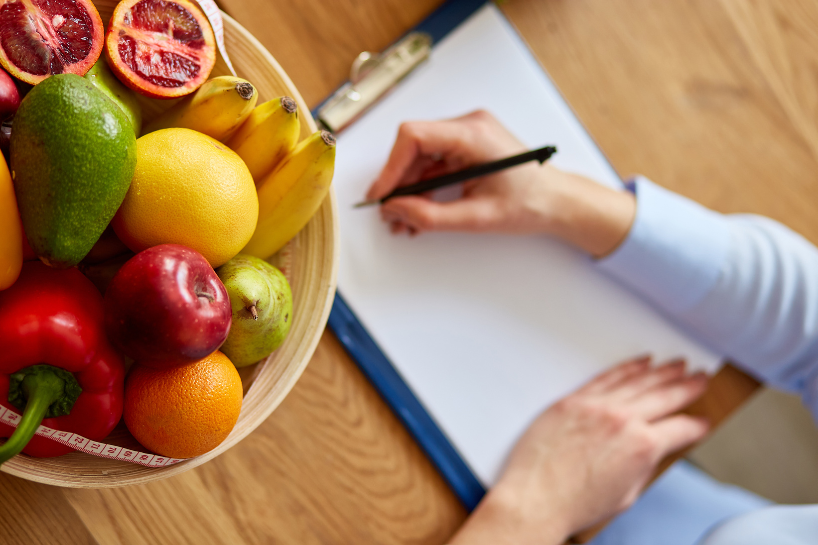 Nutritionist Writing on a Clipboard Beside a Bowl of Fruits